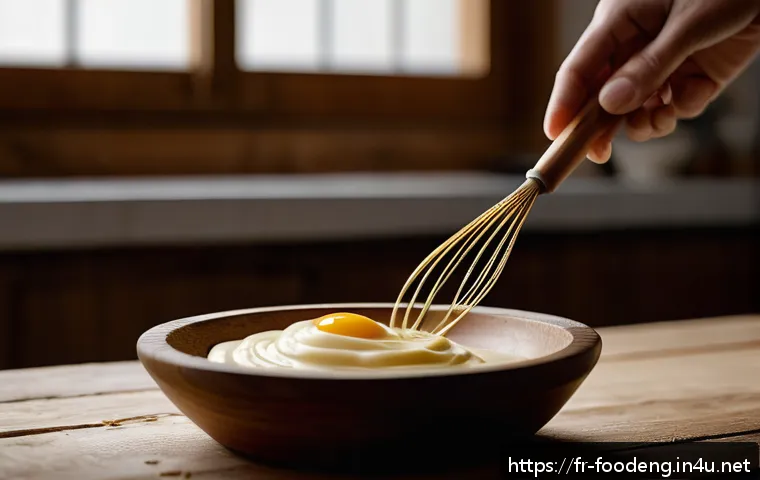 식품에서의 유화 및 분산기술 - A close-up, high-resolution image of a creamy homemade mayonnaise being whisked by hand in a rustic ...
